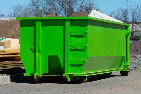 Roll-off dumpster on a construction site next to lumber